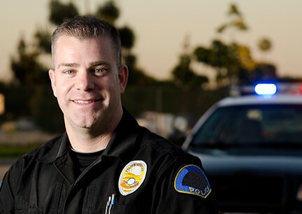 male police officer smiling with patrol car in the background